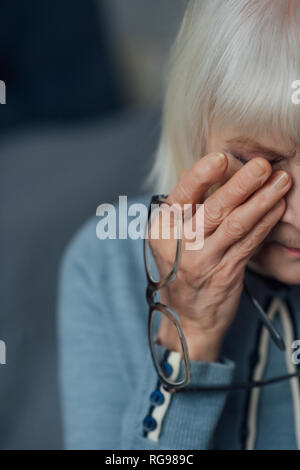 Ältere Frau mit Brille und graues Haar wischte sich und zu Hause weinen Stockfoto