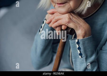 Ansicht der älteren Frau mit Händen auf Gehstock sitzen auf dem Bett zu Hause 7/8 Stockfoto