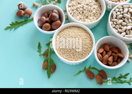 Satz von Schüsseln mit Bio Quinoa, Linsen, Kichererbsen, Weizen, Walnuss, Mandel, Haselnuss und Sesam. Getreide und Hülsenfrüchte Sortiment auf blauem Papier backgroun Stockfoto