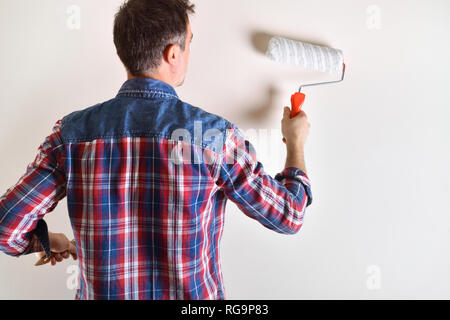 Mann mit Rolle lackieren eine weiße Wand hinter hautnah. Diy home Konzept. Vorderansicht. Horizontale Komposition. Stockfoto