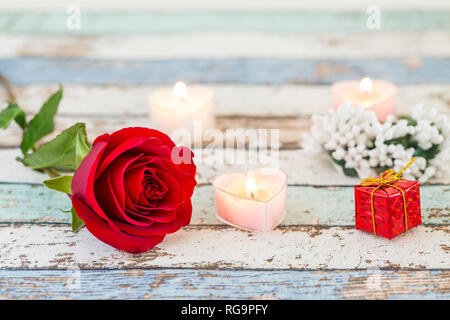 Einzelne rote Rose, Geschenkbox, Kerzen, und weiße Blumen auf Türkis Tabelle Stockfoto