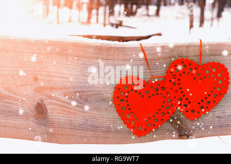 Zwei rote Herzen auf einen Jahrgang Holzbrett gegen den Winter Forest in der Sonne und Schnee. Grußkarte für Valentines Tag. Stockfoto