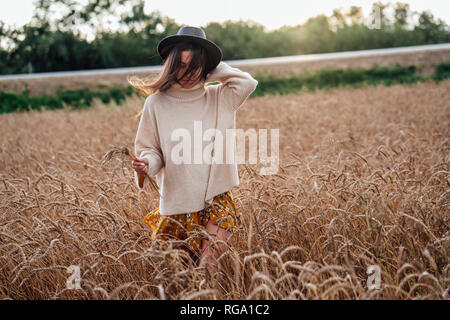 Junge Frau mit Hut und oversized rollkragen pullover Wandern in Maisfeld Stockfoto