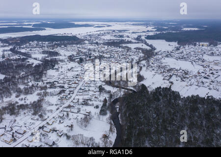 Drone Ansicht von Winter Forest, geschwungene Fluss und kleines Dorf bei bewölkter Tag Stockfoto