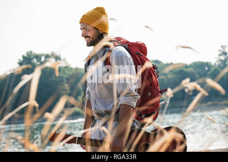 Lächelnden jungen Mann mit Rucksack und Gitarre am Flußufer Stockfoto