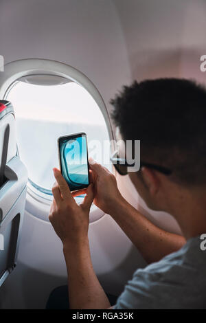 Mann im Flugzeug, sie ihr Smartphone, wobei ein Bild, Flugzeug Fenster Stockfoto