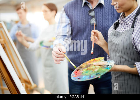 Den mittleren Abschnitt Porträt von zwei unkenntlich Künstler Holding palette Mischen der Farben beim Malen Bild auf der Staffelei in art studio, Kopie Raum Stockfoto