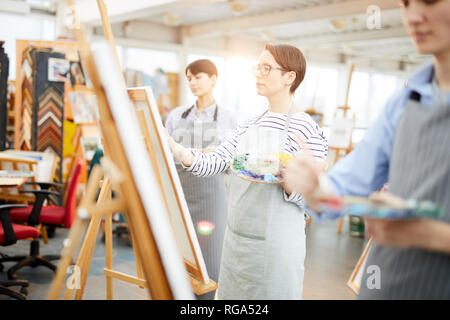 Seitenansicht Portrait von inspiriert junge Frau Malerei Bild auf der Staffelei genießen Sie arbeiten mit einer Gruppe von Studenten in art studio Stockfoto