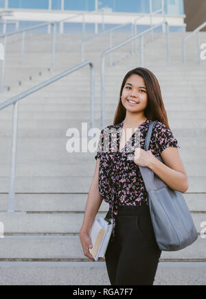 Nahaufnahme eines lächelnden jungen asiatischen Studenten holding Lehrbücher beim Stehen über die Treppe auf dem Campus Stockfoto