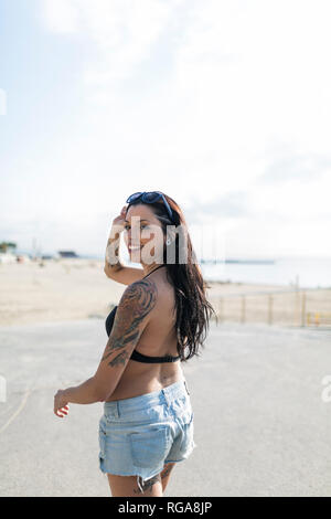 Portrait von lächelnden jungen Frau mit Nasen Piercing und Tattoos auf dem Weg zum Strand Stockfoto