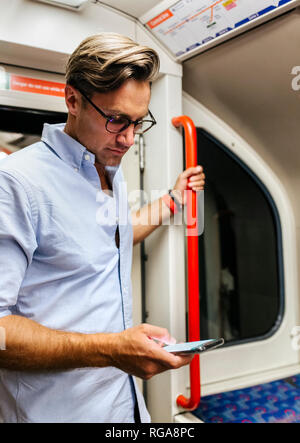 UK, London, Geschäftsmann, der in der U-Bahn an der Zelle Telefon Stockfoto