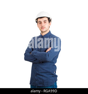 Ernsthafte selbstbewussten jungen Mann Ingenieur tragen Schutzhelm mit gekreuzten Händen Kamera auf weißem Hintergrund. Stockfoto