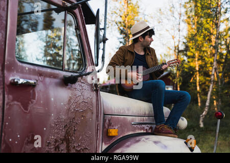 Junge amn Sitzen auf einem defekten Fahrzeug, das Spielen der Ukulele Stockfoto