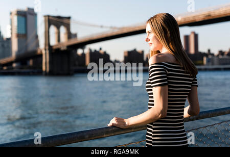 USA, New York, Brooklyn, Frau mit gestreiftem Kleid stand vor der East River bei Sonnenuntergang Stockfoto