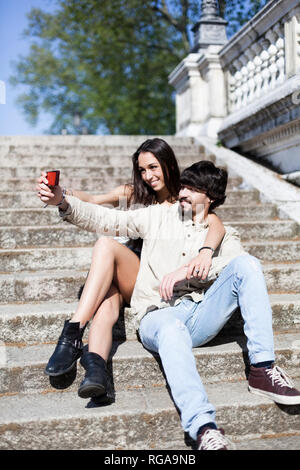 Glückliches junges Paar sitzt auf der Treppe nehmen selfie mit Smartphone Stockfoto