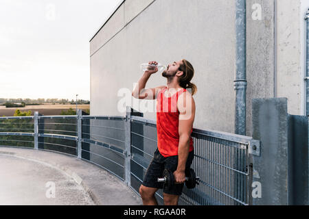 Junger Mann Trinkwasser nach dem Training mit Hanteln Stockfoto