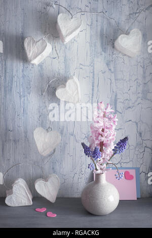 Valentines Tag oder Frühling Feier, Vase mit Hyazinthen Blumen und girlande Lichter in Form von Papier Herzen auf rustikalen Hintergrund Stockfoto