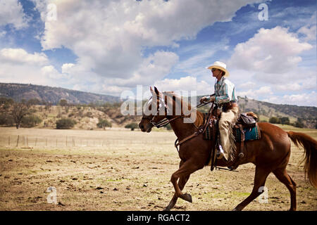 Frau mit Cowboyhut und Gamaschen reiten auf einer Ranch Stockfoto