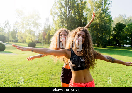 Portrait von Happy Zwillingsschwestern mit ausgestreckten Armen in einem Park Stockfoto