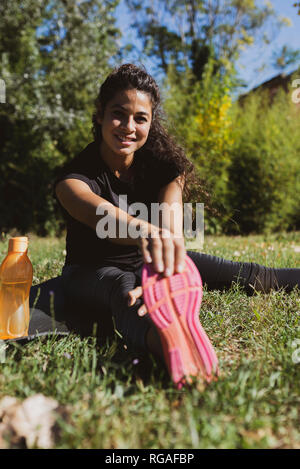 Sportliche junge Frau ihr Bein strecken auf einer Wiese Stockfoto