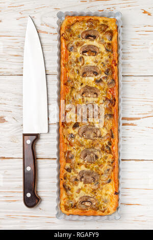 Hausgemachte Törtchen mit Champignons, Lauch, Käse und Thymian auf weißem Hintergrund im Landhausstil. Traditionelle Snacks Kuchen und ein Messer auf den Tisch. Selektiver Fokus Stockfoto