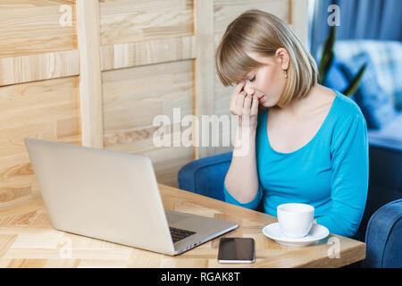 Seitenansicht Porträt der traurige junge Mädchen Freelancer mit blonden Bob Haarschnitt Haar in blaues T-Shirt im Cafe sitzen und Arbeiten am Laptop, geschlossenen Augen und Stockfoto