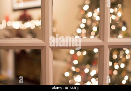 Ein bokeh Foto Peering durch französische Türen in ein Wohnzimmer für Weihnachten dekoriert. Stockfoto