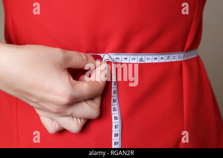 Mädchen im roten Kleid mit Maßband um die Taille. Gewichtsreduktion, abnehmen, Ernährung, Körperpflege, Kleidung Stockfoto