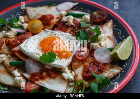 Mexikanisches Frühstück: chilaquiles, Avocado mit Ei und Gemüse close-up auf einer Platte Stockfoto