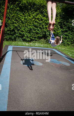 Zwei Latina Mädchen, auf Schaukeln in einem Park auf einem Spielplatz mit ihren Schatten Stockfoto