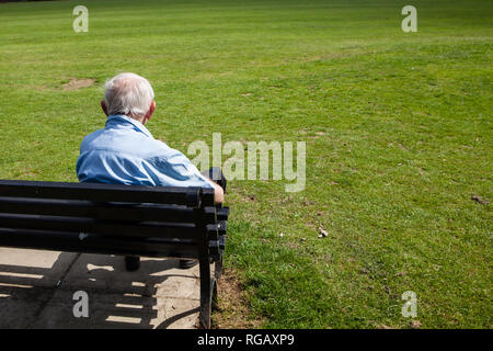 Alter Mann auf der Bank mit Blick auf einen Park im Sommer Stockfoto