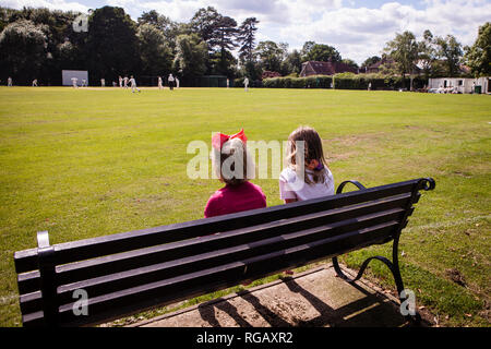 Zwei junge Mädchen auf einer Parkbank Cricket beobachten Stockfoto