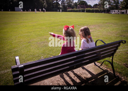 Zwei junge Mädchen auf einer Parkbank Cricket beobachten Stockfoto