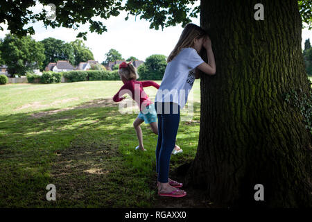 Zwei junge Mädchen spielen verstecken und in einem Park im Sommer suchen Stockfoto