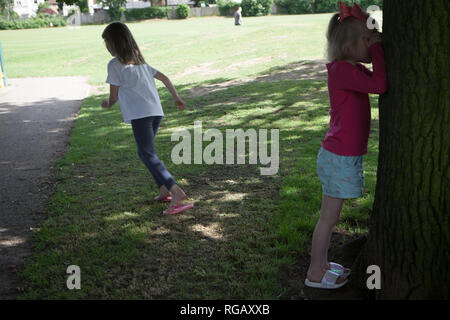 Zwei junge Mädchen spielen verstecken und in einem Park im Sommer suchen Stockfoto