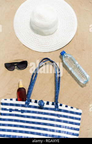 Strandtasche, Sonnencreme, Sonnenbrille und Hut auf Sand Stockfoto