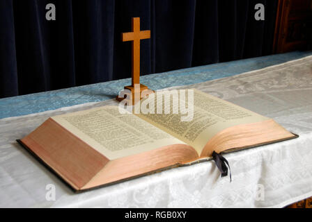 Heilige Bibel offen auf dem Tisch mit einfachen Holzkreuz hinter sich. Stockfoto