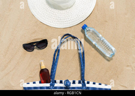 Strandtasche, Sonnencreme, Sonnenbrille und Hut auf Sand Stockfoto