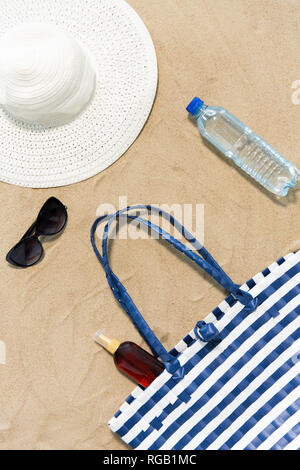 Strandtasche, Sonnencreme, Sonnenbrille und Hut auf Sand Stockfoto