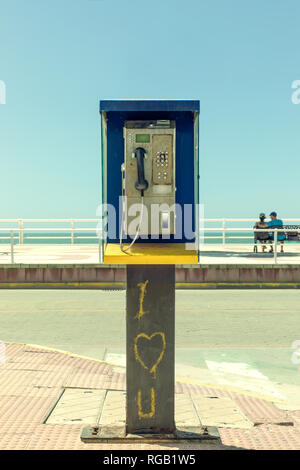 Schmutzig und ausgediente Telefonzelle mit romantischen Graffiti und ein Paar im Hintergrund. Stockfoto