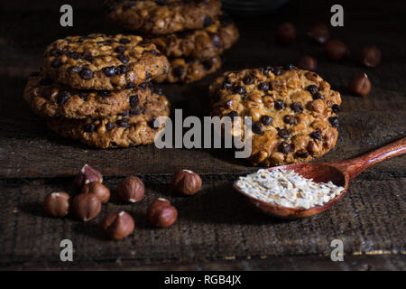 Avena cookies mit Haselnüsse und Schokolade Flocken auf einem Holztisch, und einen Löffel mit avena Flocken Stockfoto