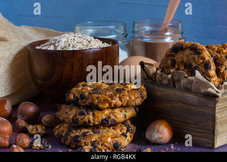 Box mit avena Cookies mit Haselnüssen, Schokolade, Chips, eine Schüssel mit avena Flocken, Gläser mit Schokolade und Mehl, Haselnüsse und ein Ei Stockfoto