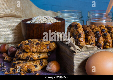 Box mit avena Cookies mit Haselnüssen, Schokolade, Chips, eine Schüssel mit avena Flocken, Gläser mit Schokolade und Mehl, Haselnüsse und ein Ei Stockfoto