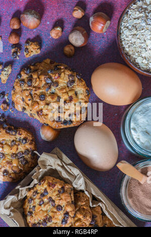 Box mit avena Cookies mit Haselnüssen, Schokolade, Chips, eine Schüssel mit avena Flocken, Gläser mit Schokolade und Mehl, Haselnüsse und zwei Eier Stockfoto