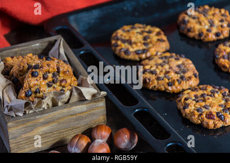 Avena cookies mit Haselnüssen und Chocolate Chips auf ein Backblech, Plätzchen in einer Box und einige Tücher Stockfoto