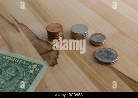 Uns Tasche änderung in kleinen Stapel zusammen mit einem gefalteten Dollarschein auf einen hölzernen Tisch angeordnet. Stockfoto