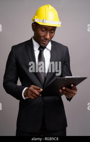 Jungen schönen afrikanischen Geschäftsmann mit hardhat gegen Grau bac Stockfoto