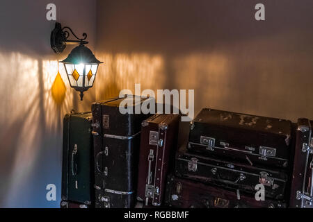 Alte Lampe leuchtet in der Dunkelheit. Alte vintage Koffer stehen in einem Stapel Stockfoto