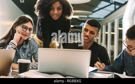 Vier Studenten mit Laptop für Forschung an der Bibliothek. Gruppe von Studenten lächelnd und mit Laptop in der Universitätsbibliothek. Stockfoto