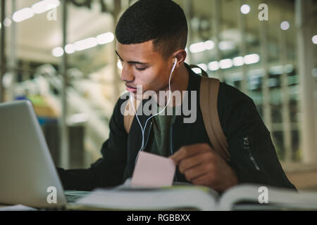 Männliche Kursteilnehmer sitzen Notizen mit Laptop auf dem Tisch Vorbereitung von Hausarbeiten. Junge Menschen studieren an der Hochschule Bibliothek. Stockfoto